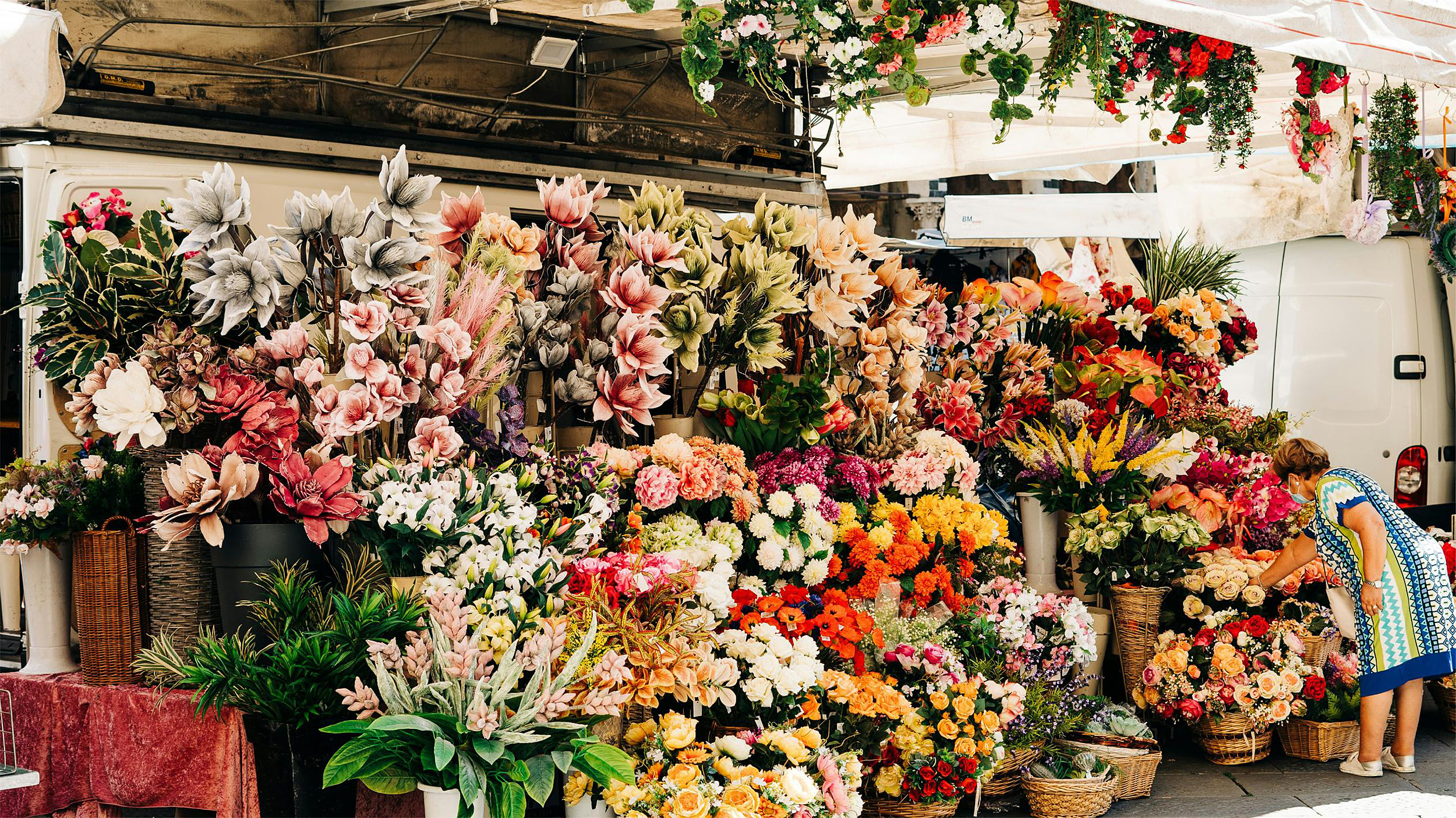 A Spring Farmers' Market in the Mediterranean. A woman selects roses from an abundant flower stand. 